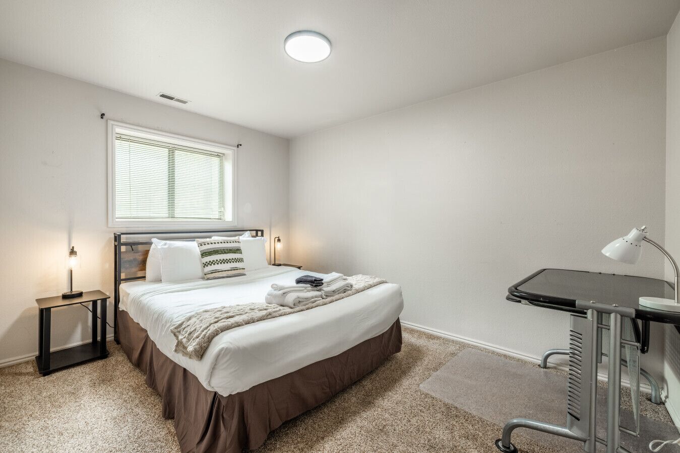 Une chambre à coucher avec un lit, des lampes de chevet, une fenêtre, un bureau et une chaise.
