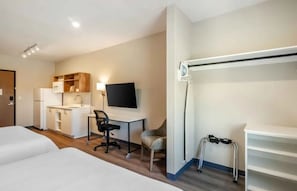 Habitación de hotel con cama, kitchenette, escritorio, silla, televisor y un apoyo para caminar.