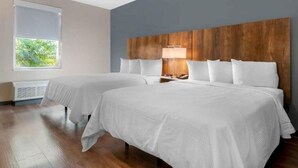 Une chambre d’hôtel avec deux lits, une tête de lit en bois, une fenêtre avec des stores et une table de chevet avec une lampe.