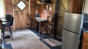 A rustic kitchen with wooden walls, a refrigerator, and a dining area with chairs and a table.
