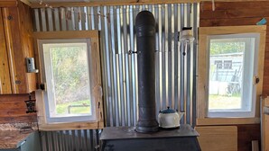 A wood-burning stove with two control knobs, a metal pipe, and a kettle on top.