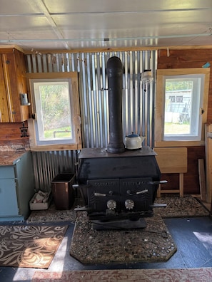 A wood-burning stove with two control knobs, a metal pipe, and a kettle on top. - 2-bedroom off grid remote cabin near Bigfork perfect for a relaxing getaway. (Bigfork)