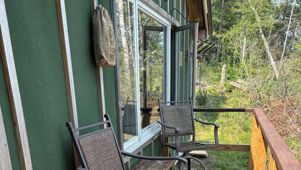 A wooden deck with two metal chairs and a red table, surrounded by a green wall and a wooden railing.