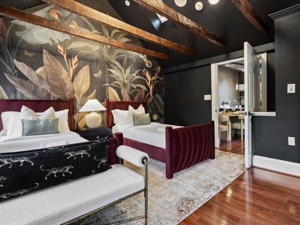 Una camera da letto con un letto grande, un letto più piccolo, una scrivania e un bagno visibile attraverso una porta aperta.