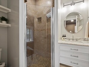 Un bagno con cabina doccia in vetro, uno specchio rotondo e un mobile vanit脿 bianca con cassetti.