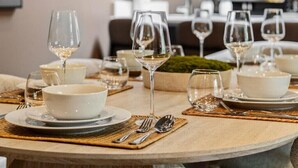 Une table à manger dressée avec des bols blancs, des verres à vin et des couverts, avec une cuisine en arrière-plan.