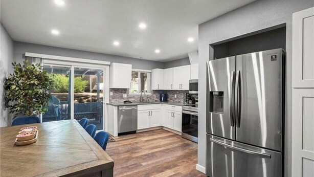 Una cocina moderna con un refrigerador de acero inoxidable grande, armarios blancos y una mesa de comedor de madera con sillas.
