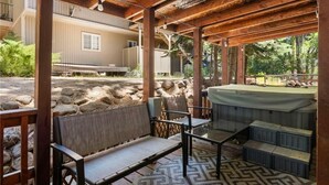 Un espacio de estar al aire libre techado con un jacuzzi, paredes de piedra y vista a un edificio.