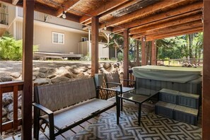 A covered outdoor seating area with a hot tub, stone walls, and a view of a building.
