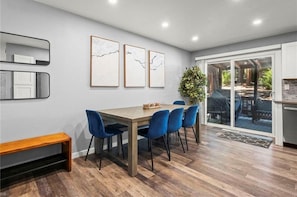 A dining area with a wooden table, blue chairs, and framed artwork on the wall.