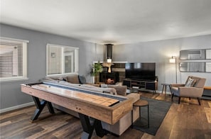 A modern living room with a pool table, a sofa, a TV, and a fireplace.