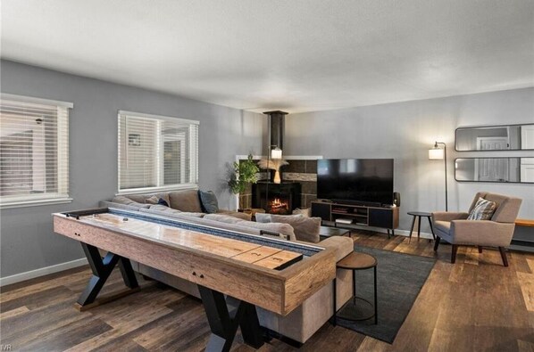 A modern living room with a pool table, a sofa, a TV, and a fireplace.