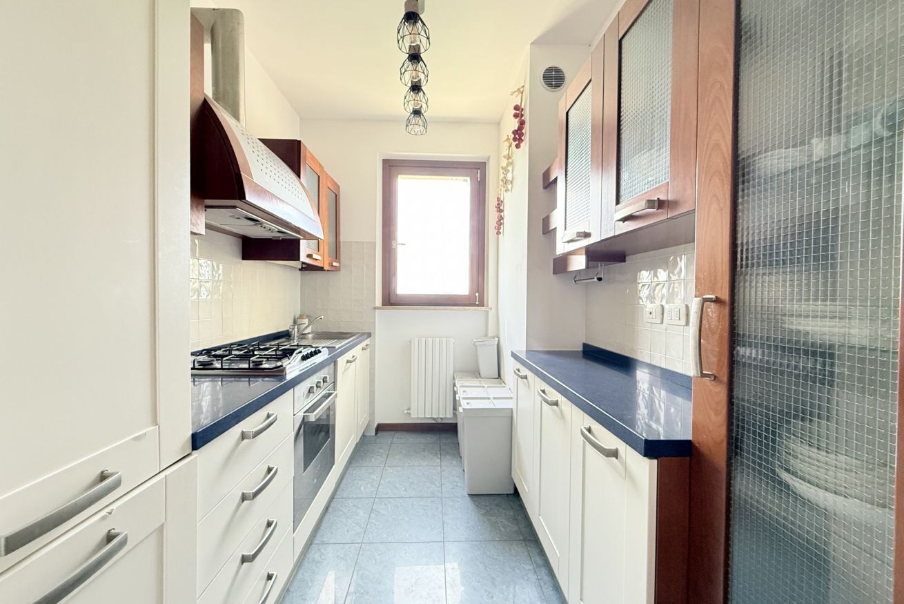 A narrow kitchen with white cabinets, a blue countertop, a gas stove, and a window.