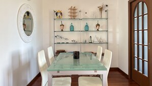 A dining area with a glass table and white chairs, a mirrored wall, and a wooden door with glass panels. - N317 - Numana, two-bedroom apartment with panoramic view (Numana)