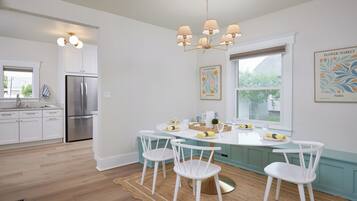 Una cocina moderna con armarios blancos, un refrigerador de acero inoxidable, una mesa de comedor con sillas y una araña.
