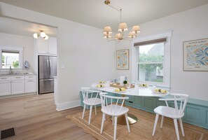 A modern kitchen with white cabinetry, a stainless steel refrigerator, a dining table with chairs, and a chandelier. - Blue Gables 1920s Craftsman Near WWU 4BR 3BA Sleeps 9 Fenced Yard (College Place)