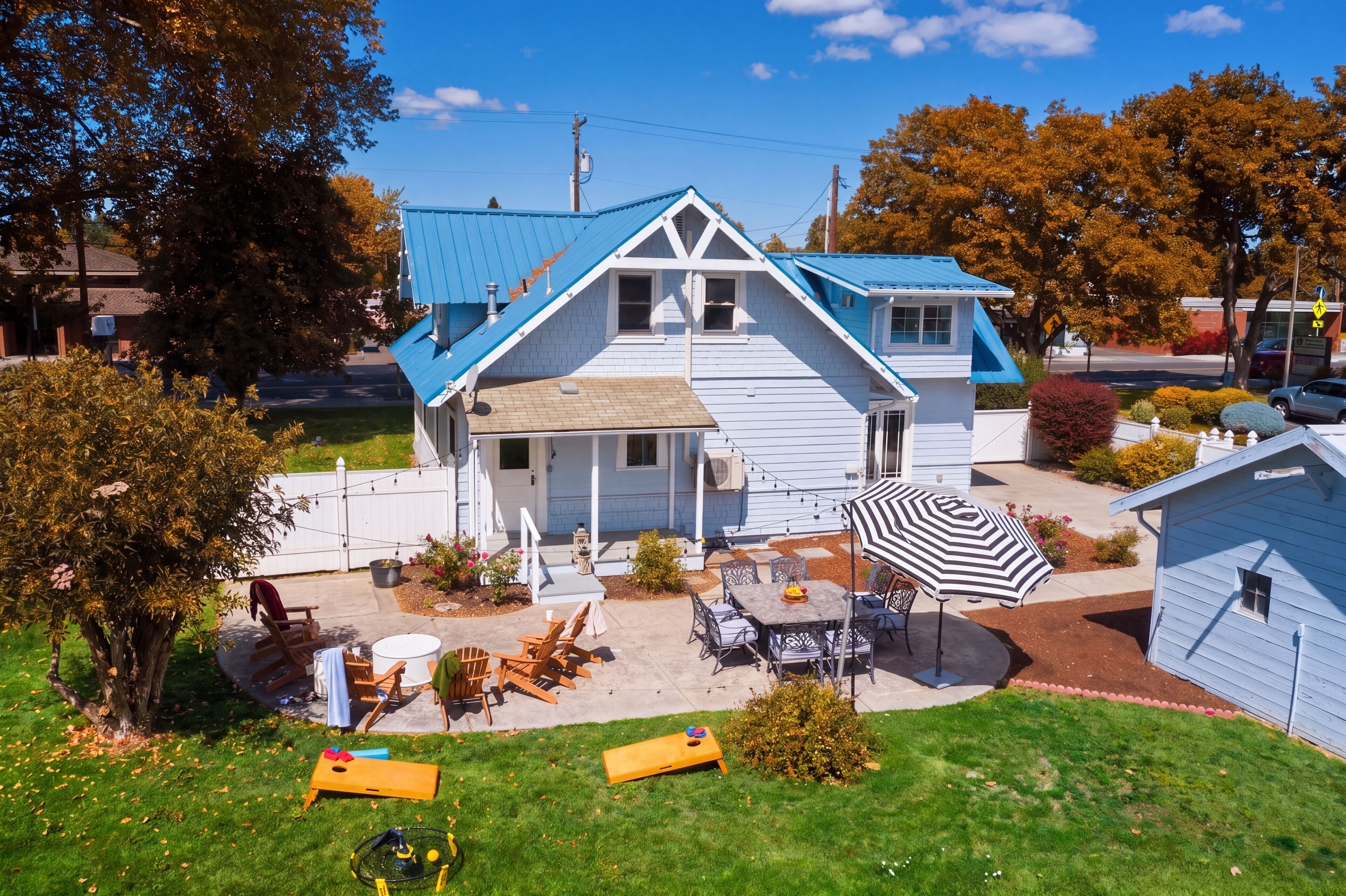 Une maison à deux étages avec un toit bleu, une véranda dotée de sièges extérieurs et un petit jardin.
