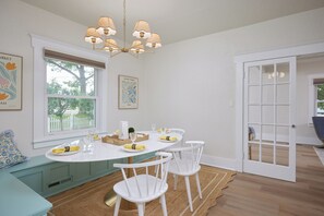A dining area with a round table, white chairs, a chandelier, and a view of a white picket fence outside. - Blue Gables 1920s Craftsman Near WWU 4BR 3BA Sleeps 9 Fenced Yard (College Place)