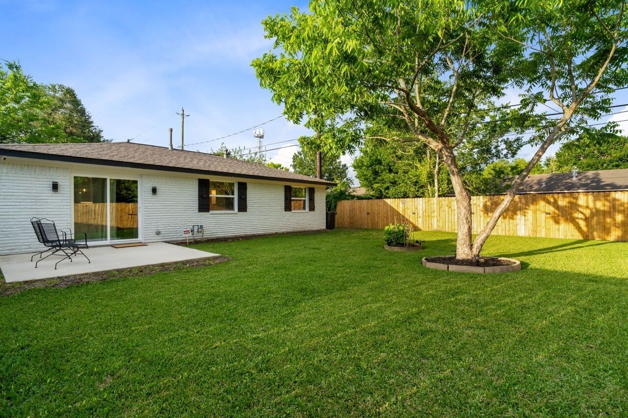 Une maison de plain-pied avec un patio couvert, une pelouse et une clôture en bois.