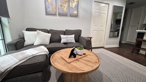 A living room with a grey sofa, a round wooden coffee table, and a 'welcome home' pillow.