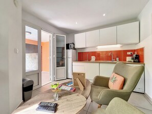 A compact living space with a kitchenette, a dining area with a table and chairs, and a sliding glass door leading to a balcony. - Le Cardinal - Jacuzzi - Terrasse – AC (Les Avirons)
