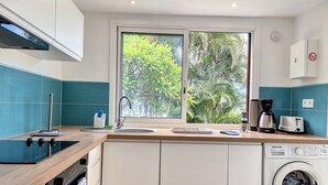 Eine moderne Küche mit integriertem Waschmaschine, einem Fenster mit Blick auf Grünflächen und einer Kaffeemaschine.