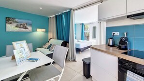 Ein kleines Hotelzimmer mit Bett, Schreibtisch mit Stuhl, einer Küchenzeile und Blick ins Freie.