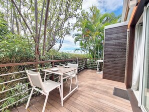 A wooden deck with a table and chairs, surrounded by lush greenery and a view of the sky. - Aybowan - Jacuzzi - Climatisation (Les Avirons)