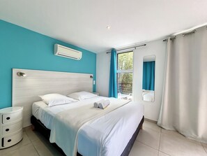 A bedroom with a bed, a bedside table, an air conditioning unit, and a window with curtains. - Aybowan - Jacuzzi - Terrasse - AC (Les Avirons)