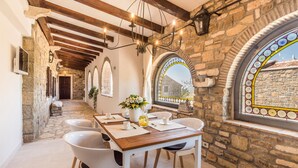 Et rum med stenvægge, et træbord, stole og en lysekrone.