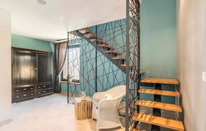 Ein Zimmer mit Treppe, einem weißen Korbstuhl, einem Holztisch und einem dunklen Holzschrank.