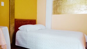 Un lit simple avec une tête de lit en bois, dans une pièce aux murs jaunes et à un mur blanc uni agrémenté d’une partie texturée.