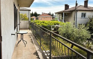 Ein Balkon mit Tisch, Metallgeländer und Blick auf Nachbarhäuser und Grünflächen.