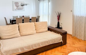 Ein Wohnzimmer mit einer Couch, einem Esstisch mit Stühlen, einer Vase mit Blumen und einem Bild an der Wand.