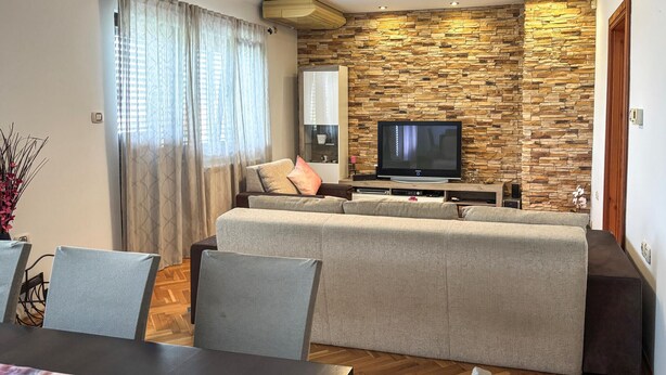 A modern living room with a stone wall, a flat-screen TV, a sofa, and a dining area with chairs. - 3 bedroom amazing apartment in Kostrena (Kostrena)