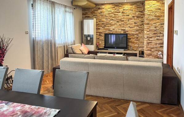Ein modernes Wohnzimmer mit Steinwand, Flachbildfernseher, Sofa und Essbereich mit Stühlen.