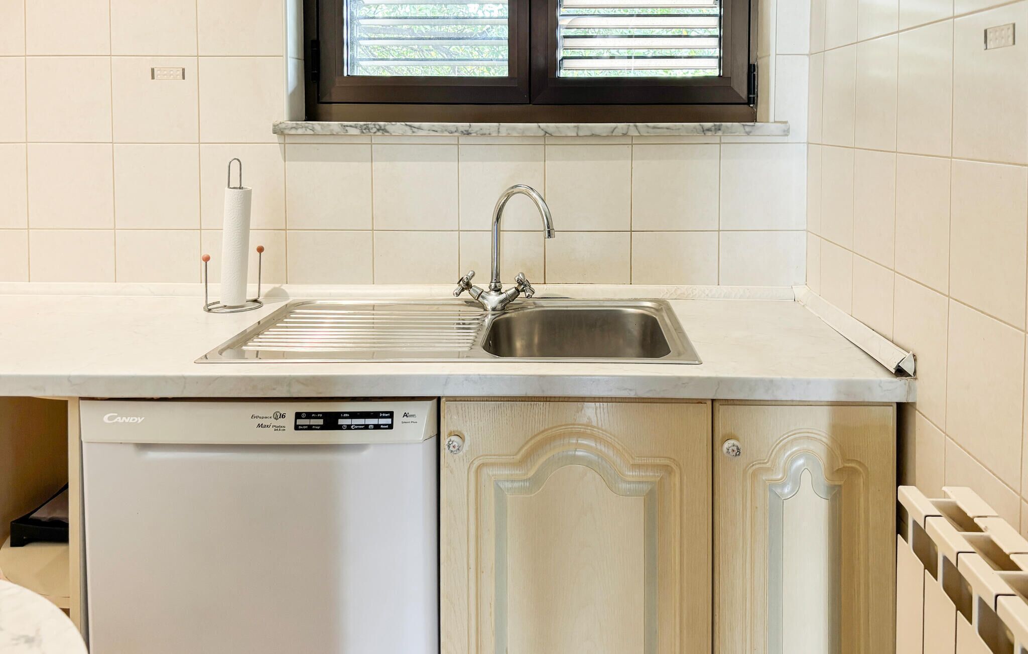 A kitchen with a dishwasher, a sink, and a window with blinds.