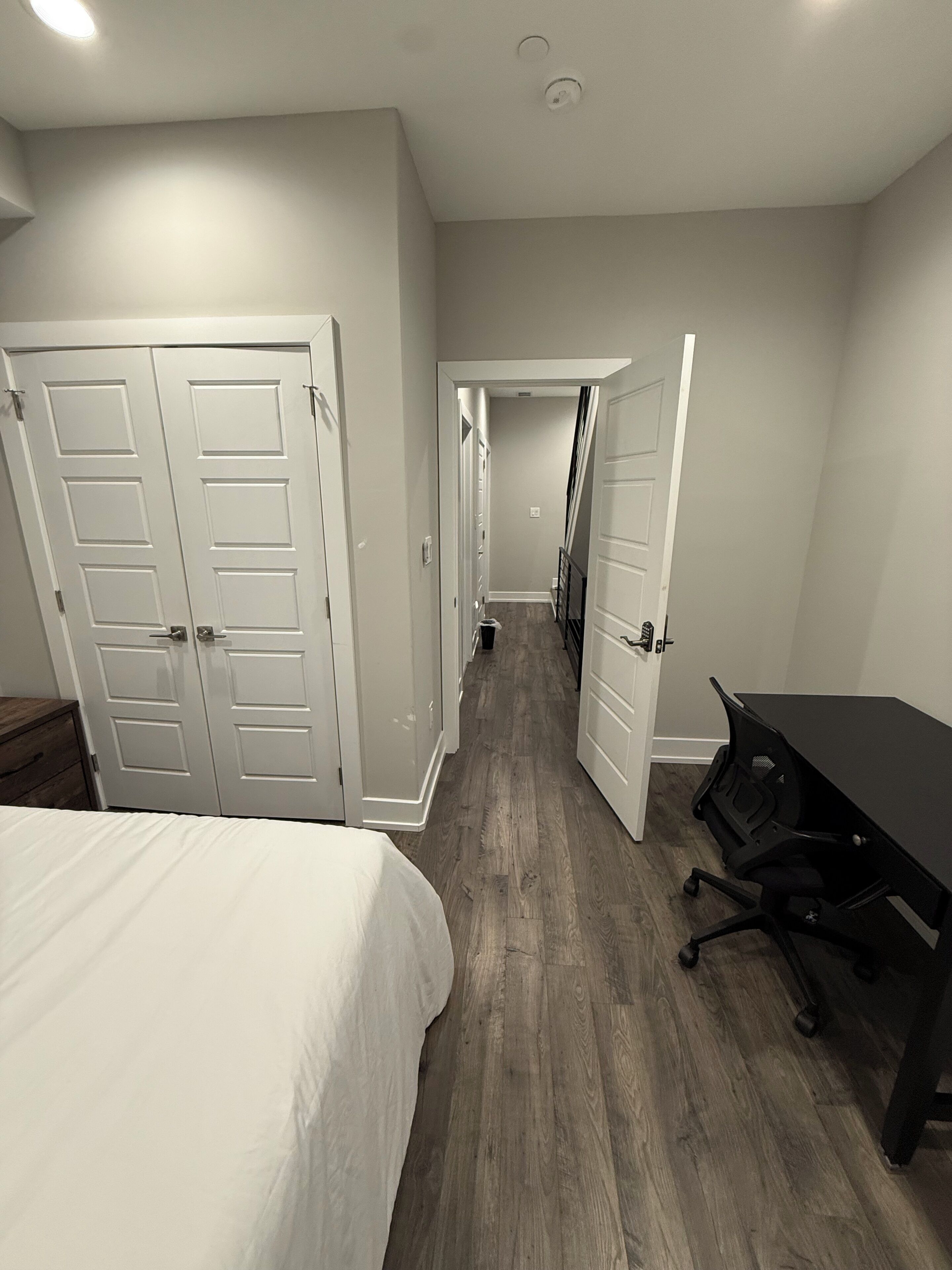 Een slaapkamer met een bed, een bureau en een stoel. Er zijn twee deuren naar andere kamers.