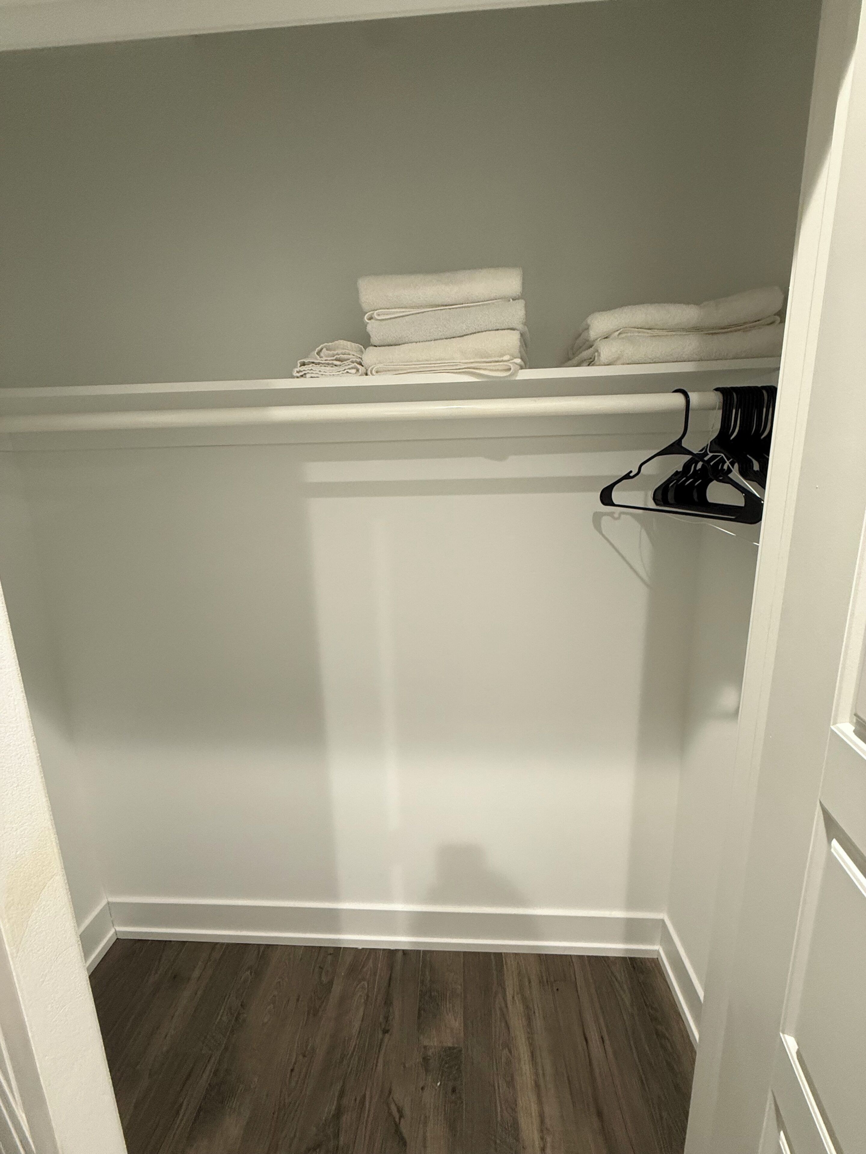 A closet with folded towels, a hanging rack, and a wooden floor.