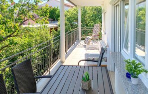 Un balcon agrémenté de meubles en osier, d’une plante en pot et offrant une vue sur la verdure et les bâtiments.