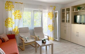 A living room with two chairs, a small table, a sofa, and a TV.