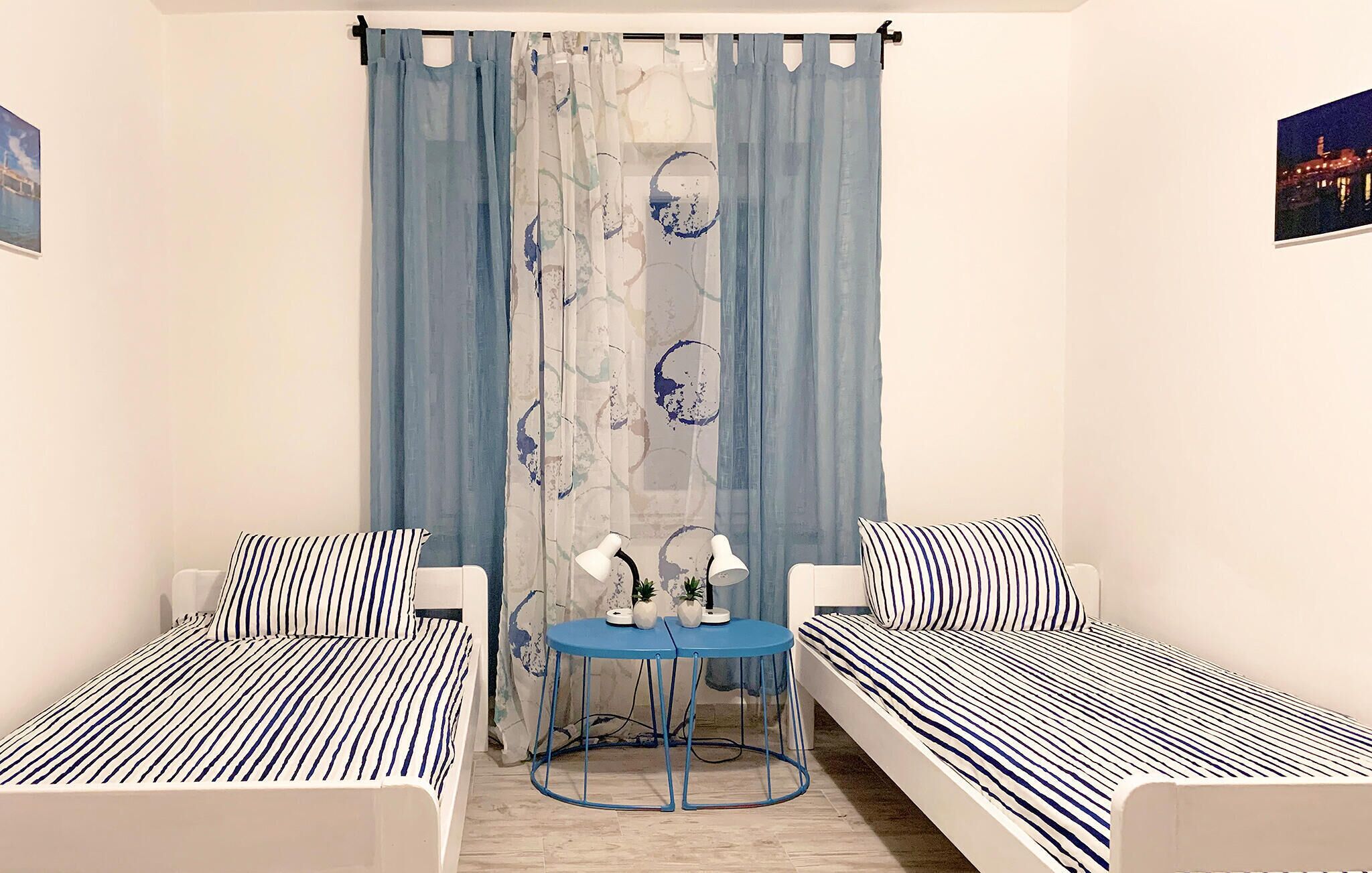 A room with two single beds, a small table with two lamps, and a curtain with a floral pattern.