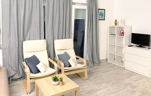 A living room with two beige armchairs, a wooden coffee table, a TV on a white cabinet, and patterned curtains. - Beautiful apartment in Krk with WiFi (Krk)