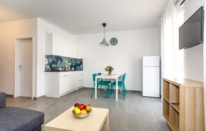A modern kitchen with white cabinets, a dining table with teal chairs, a fruit bowl on a coffee table, and a TV mounted on the wall. - 1 bedroom nice apartment in Krk (Krk)