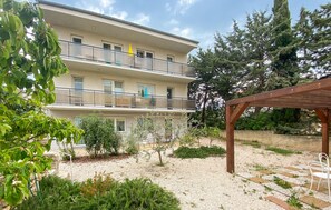 A multi-story building with balconies, a garden area with gravel and plants, and a wooden pergola. - 1 bedroom nice apartment in Krk (Krk)