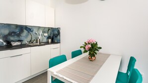 Una cocina moderna con armarios blancos, salpicadero negro y un comedor con sillas azul turquesa y una mesa blanca.