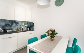 A modern kitchen with white cabinets, a black backsplash, and a dining area with teal chairs and a white table. - 1 bedroom nice apartment in Krk (Krk)