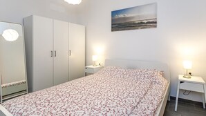 Un dormitorio con cama, armario, mesita de noche con lámpara y un cuadro en la pared.