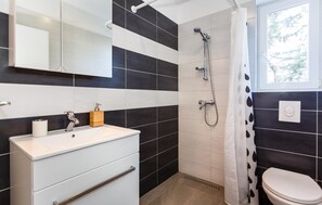 Ein Badezimmer mit einem weißen Waschbecken, einem Spiegel, einer Dusche und einer Toilette.