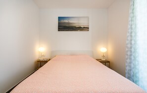 Ein Schlafzimmer mit einem Bett, zwei Nachttischen, einem Wandbild und einem Fenster mit Vorhang.
